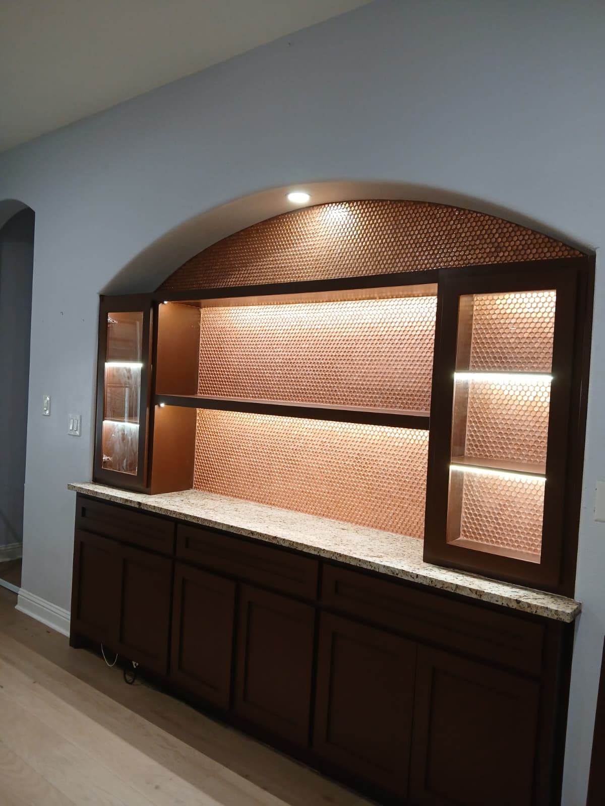 Completed custom arched built-in with dark cabinetry, stone counter, and illuminated shelving