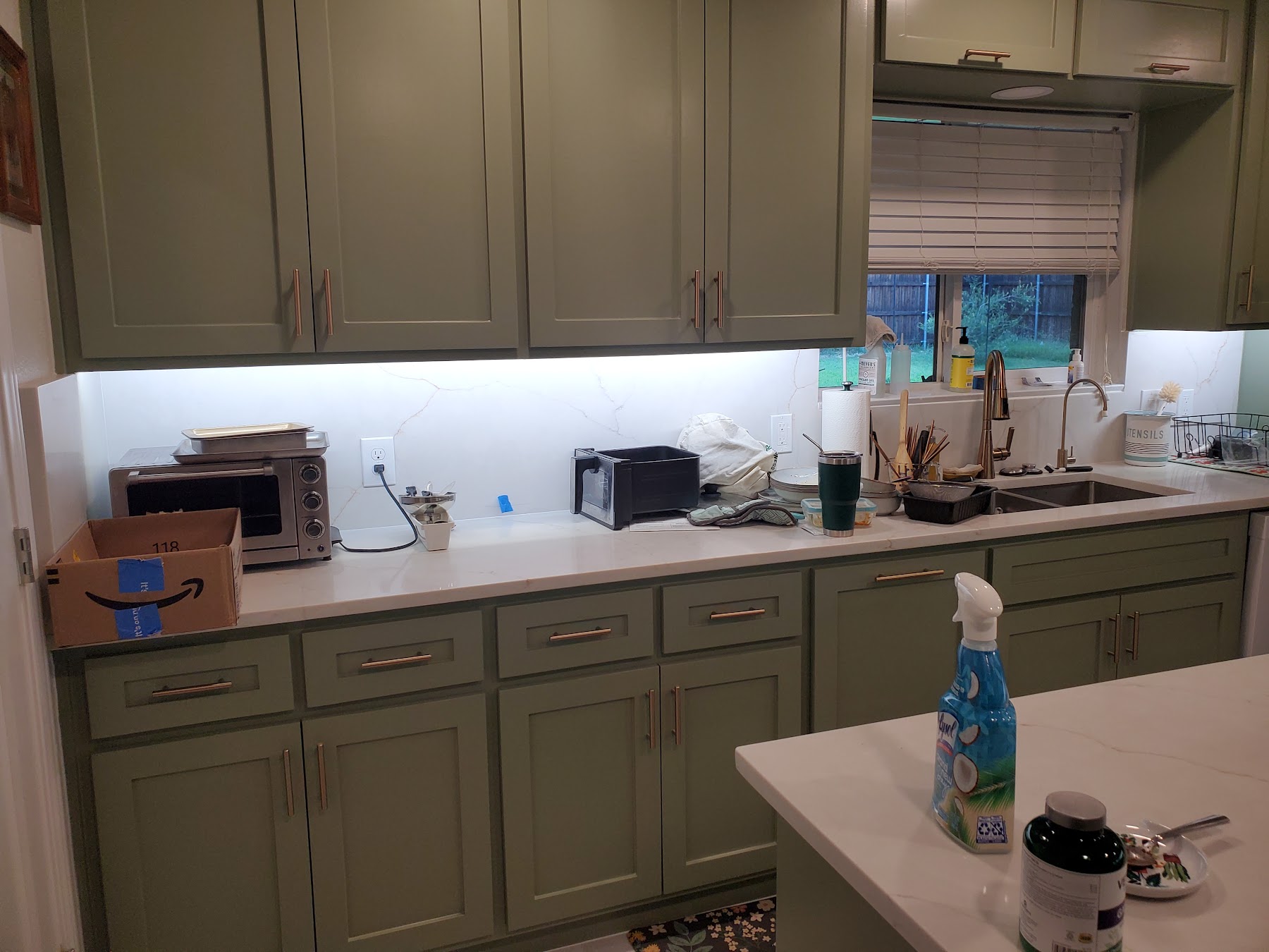Wide view of green kitchen cabinets and updated counters