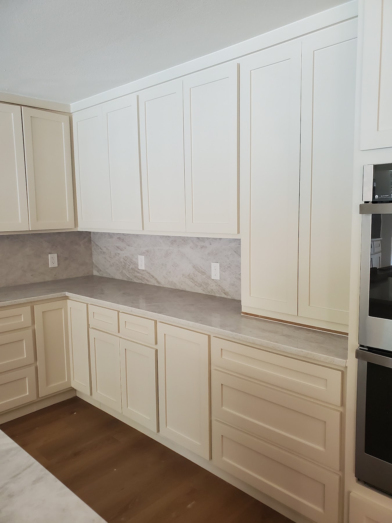 Completed white kitchen cabinetry with tile backsplash and wood flooring